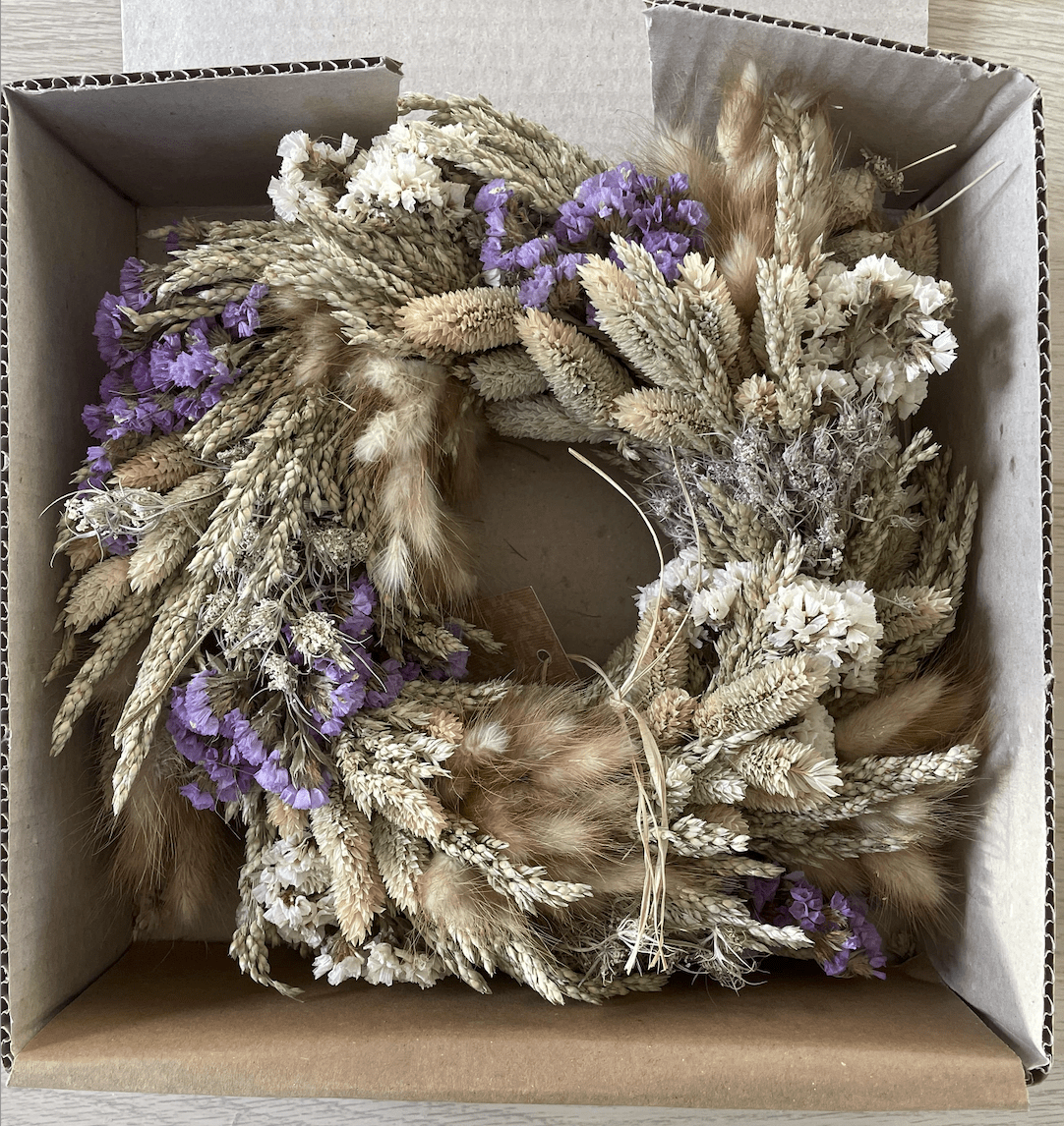 Dried floral wreath with purple flowers and fur accents in a cardboard box.
