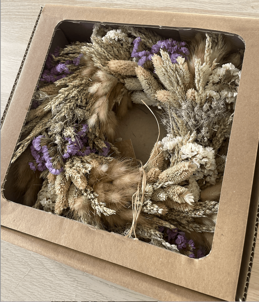 Dried floral wreath in a cardboard box on a wooden surface