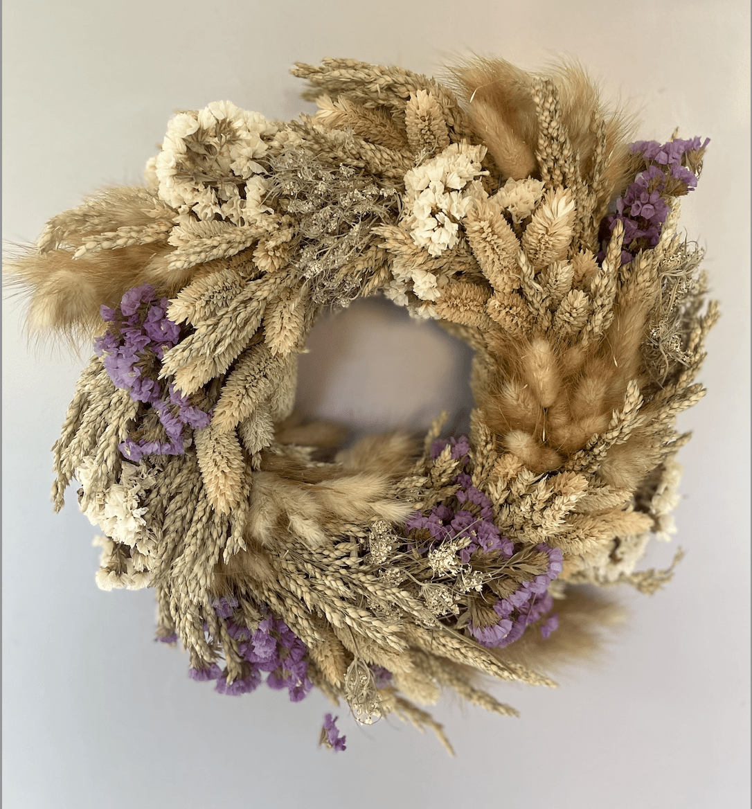 Wreath made of dried flowers and grasses with purple accents on a light gray background