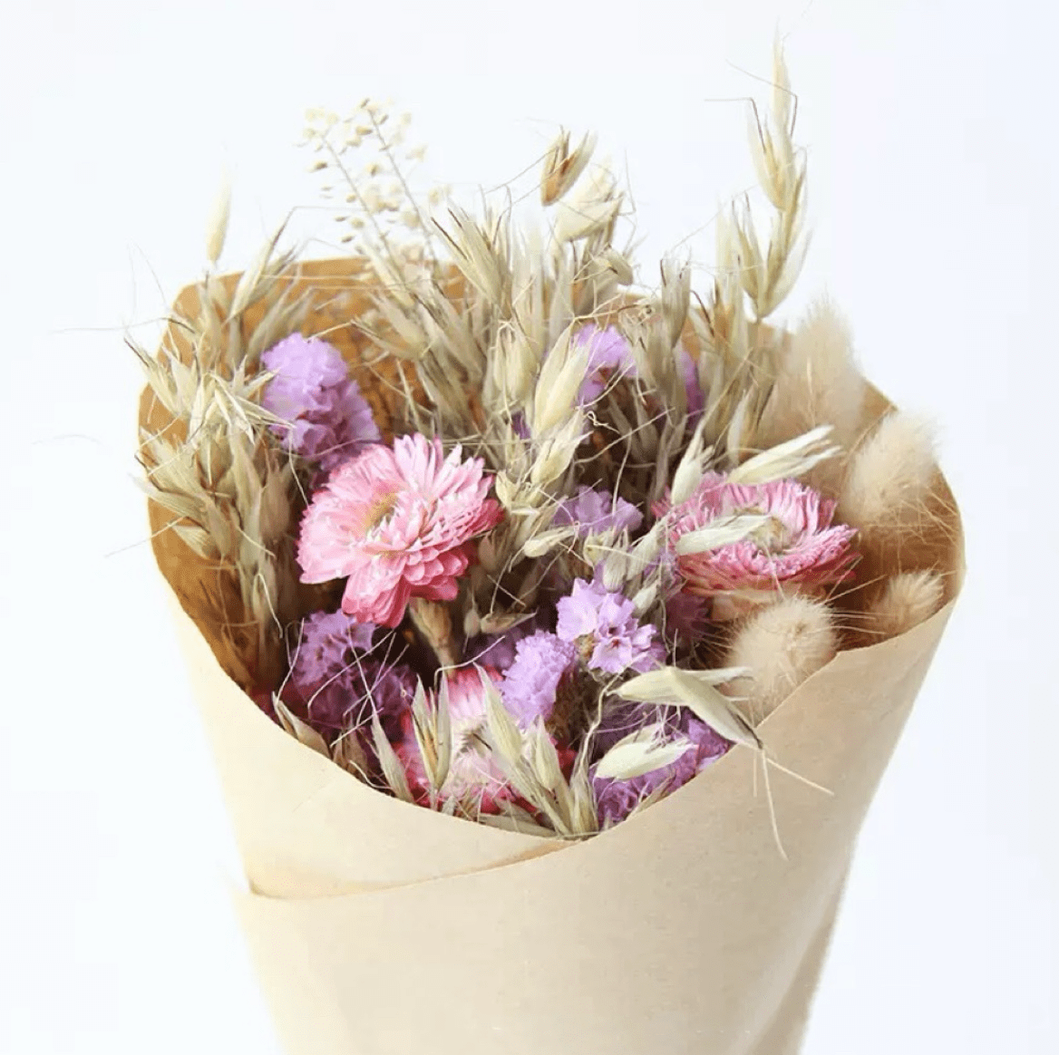 Bouquet of pink and purple flowers with dried elements in a beige paper wrap on a white background