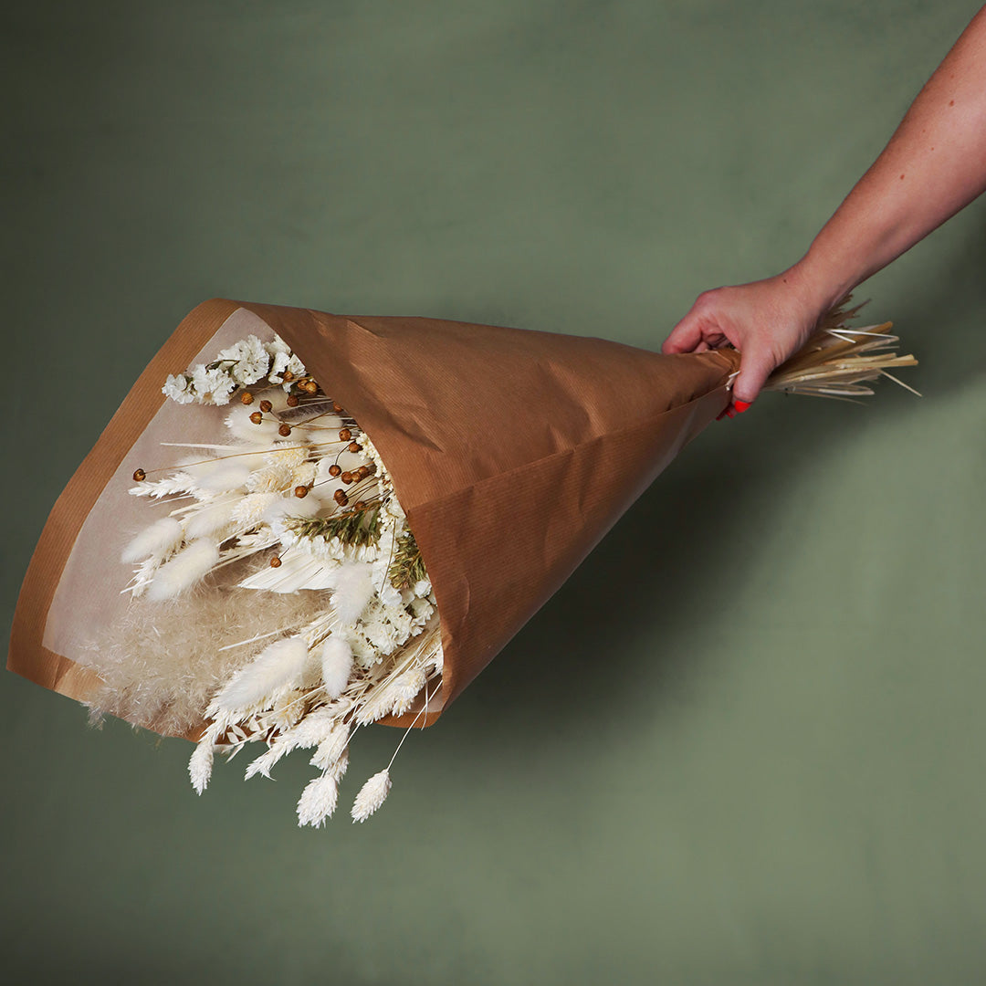 Bouquet of dried flowers wrapped in brown paper held by a hand on a green background