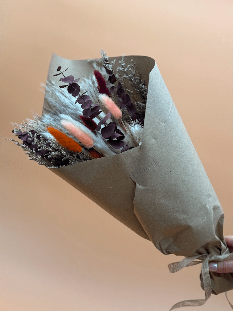 Bouquet of dried flowers wrapped in brown paper against a beige background