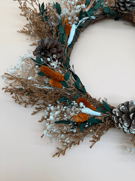 Decorative wreath with dried foliage, pinecones, and flowers on a light background