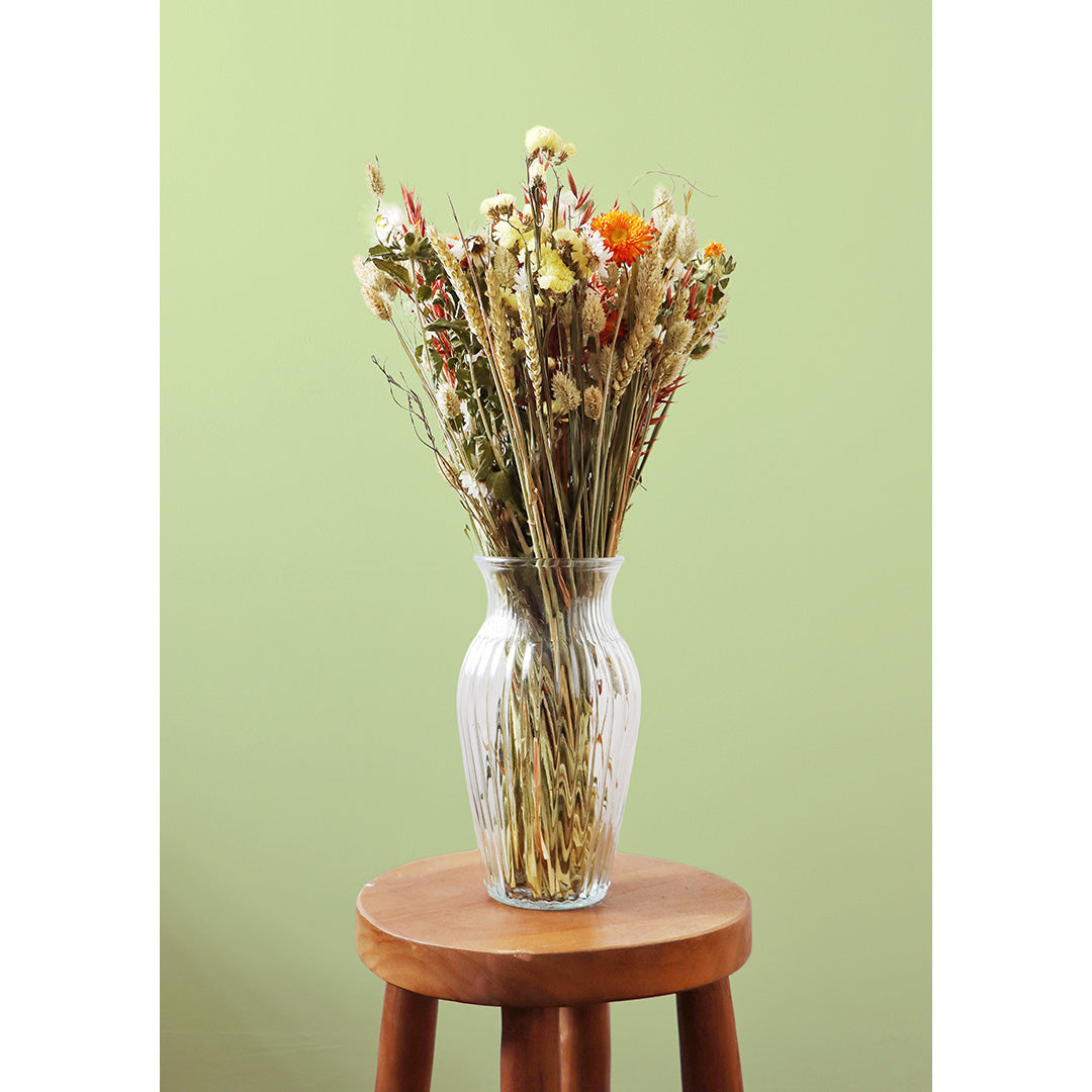 Clear glass vase with dried flowers on a wooden stool against a light green background