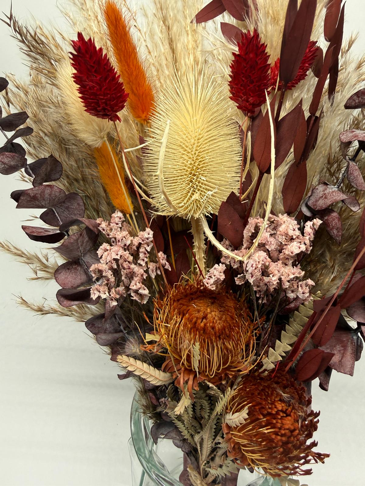 Dried floral arrangement with brown, red, and beige tones on a light gray background