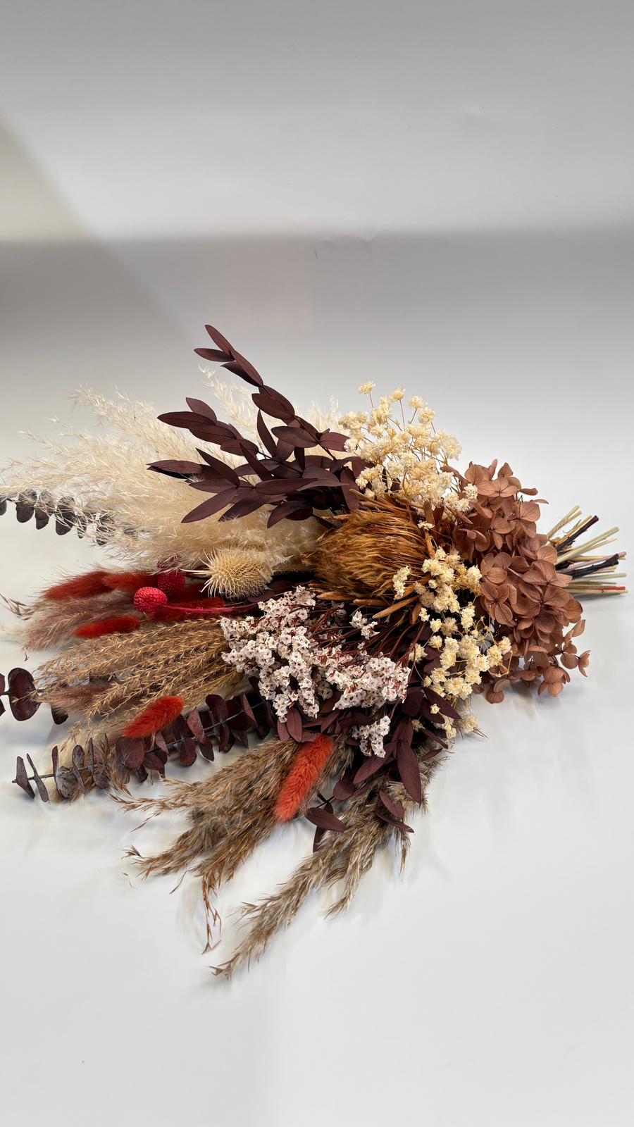 Dried floral arrangement with brown, red, and beige tones on a light gray background