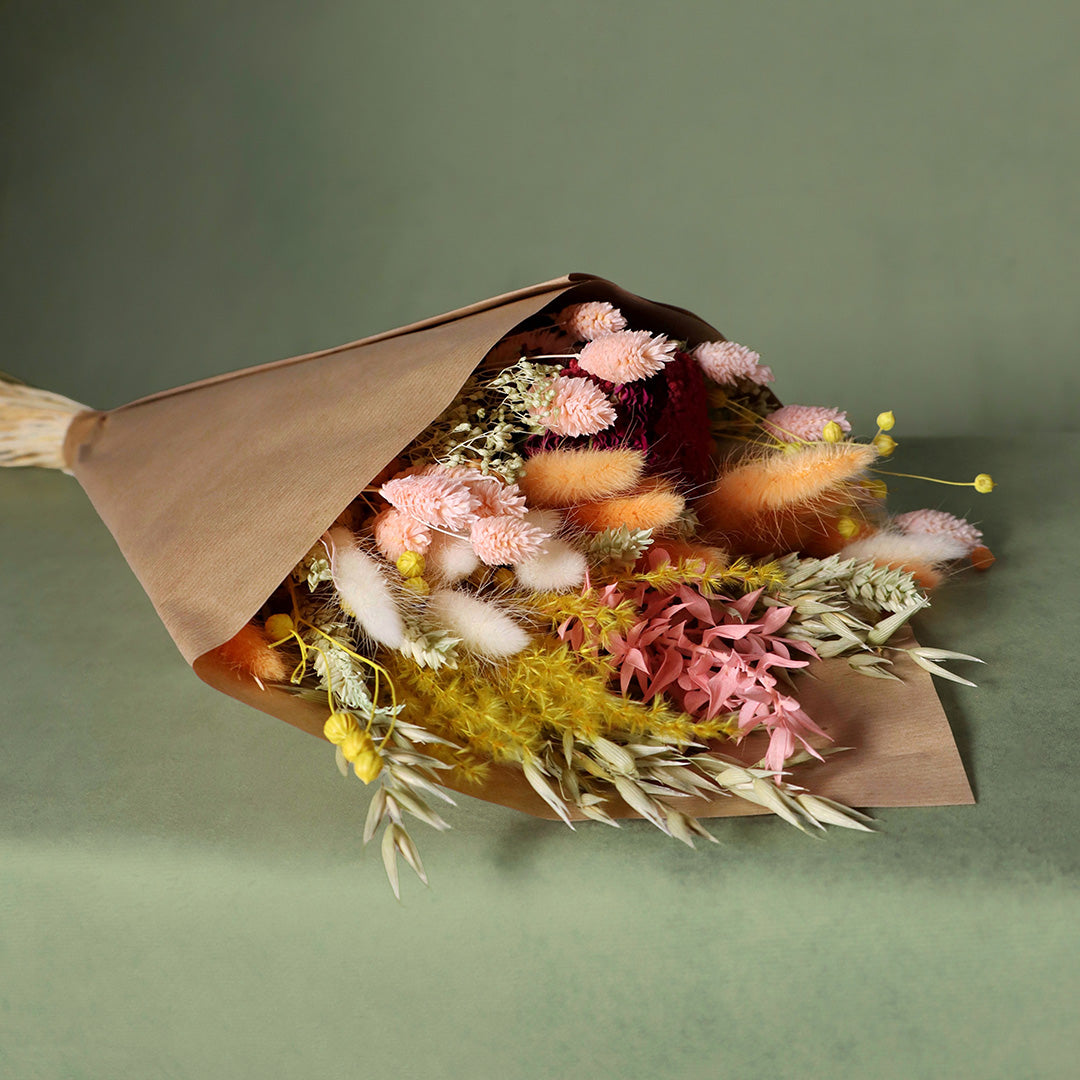 Bouquet of dried flowers wrapped in brown paper on a green background