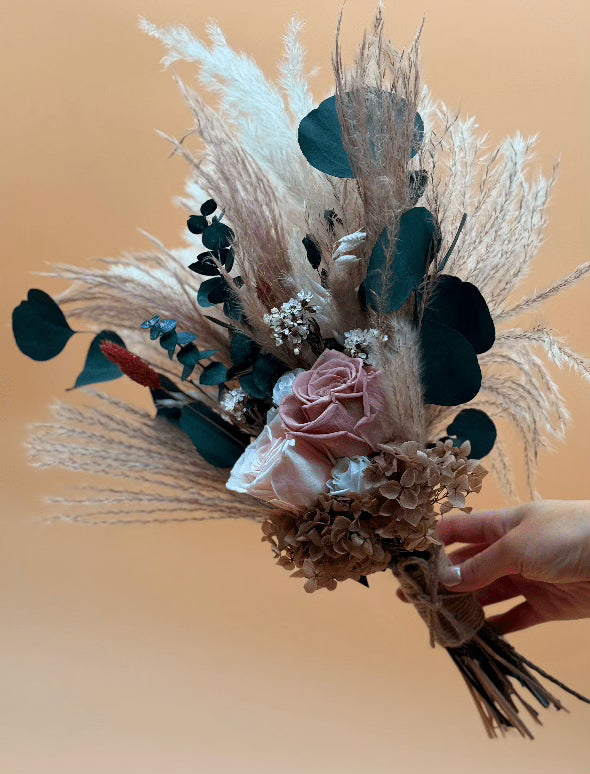 Bouquet of dried flowers and greenery held by a hand against a beige background