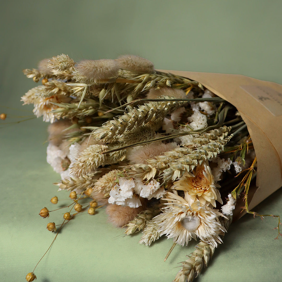 Bouquet of dried flowers wrapped in brown paper on a green background
