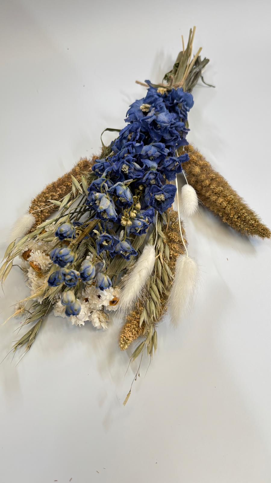 Decorative arrangement with dried blue flowers, brown leaves, and feathers on a white background