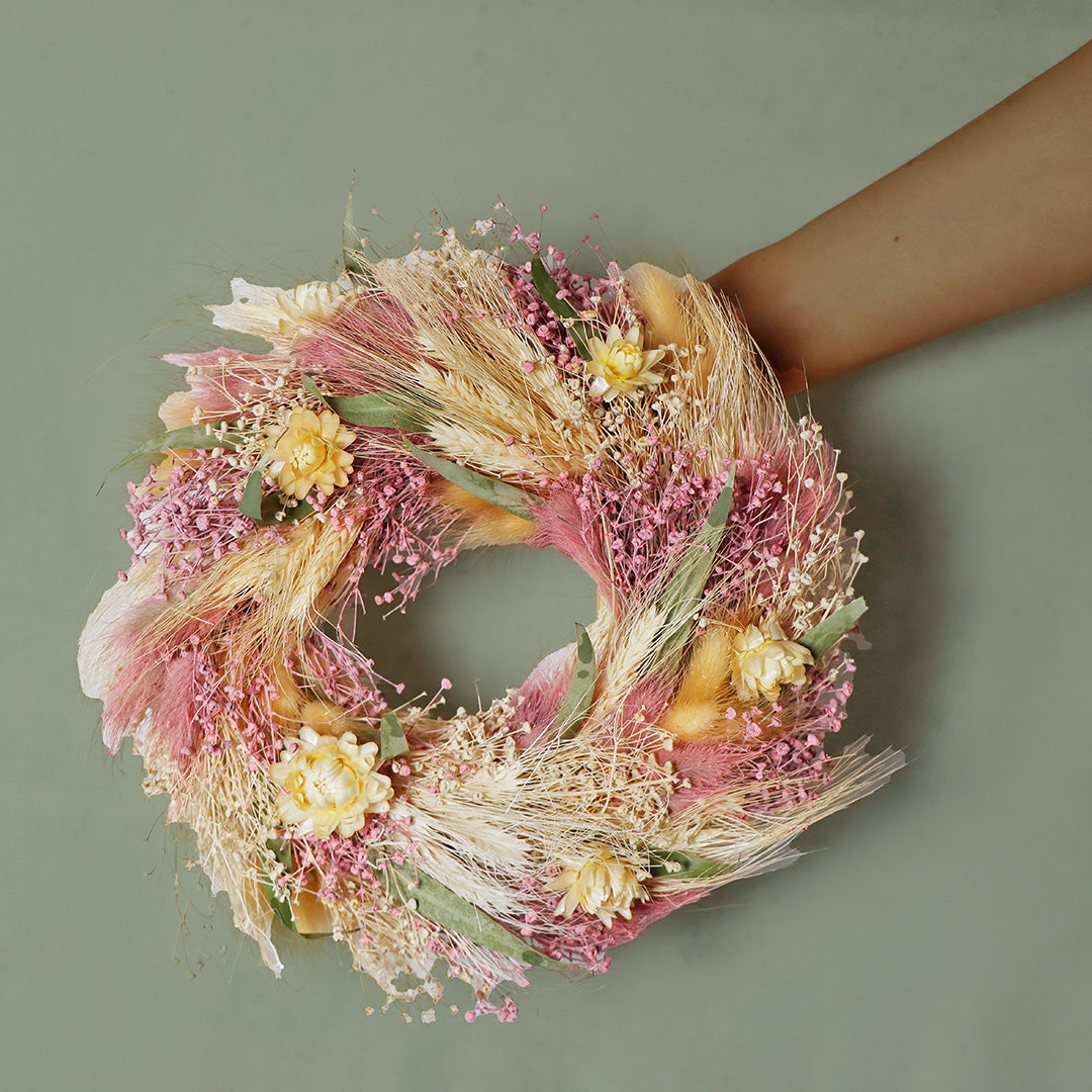 Decorative wreath with pink, yellow, and green flowers on a plain background