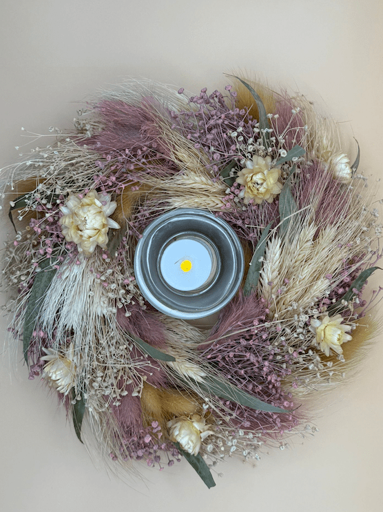 Decorative wreath with dried flowers and a candle holder on a light background