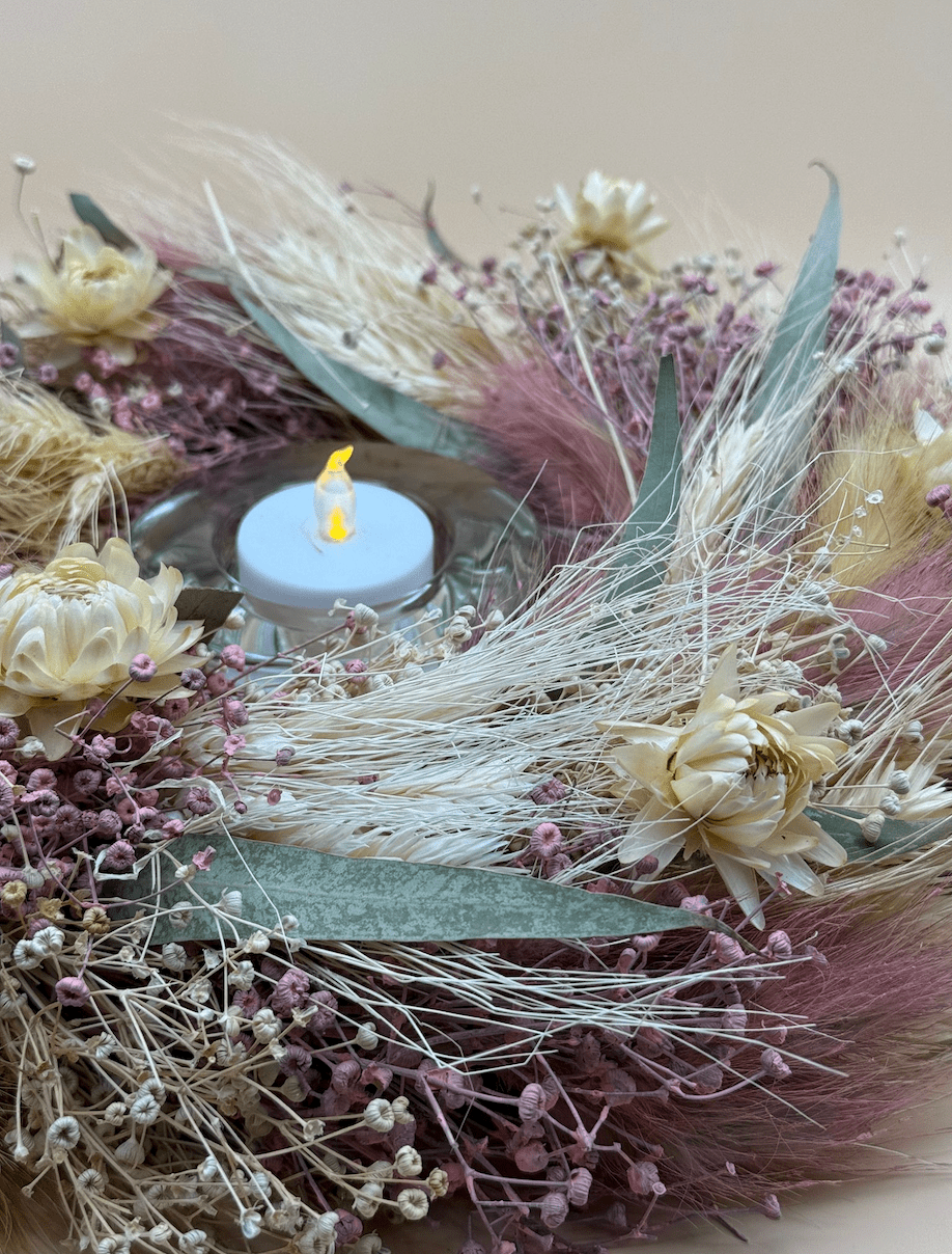 Decorative arrangement with dried flowers, a candle, and feathers on a neutral background