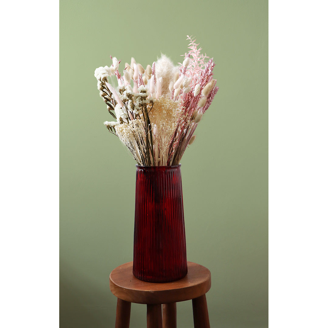 Red vase with dried flowers on a wooden stool against a green background