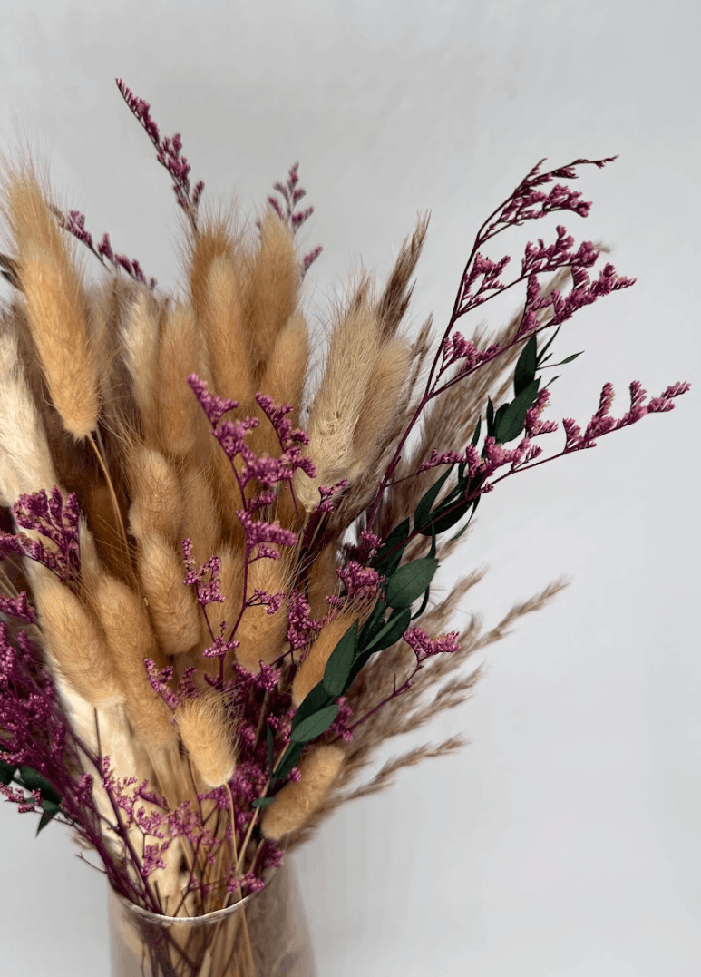 Boho dried flower arrangement with pampas grass, pink dried flowers, and eucalyptus in a clear glass vase on a light background
