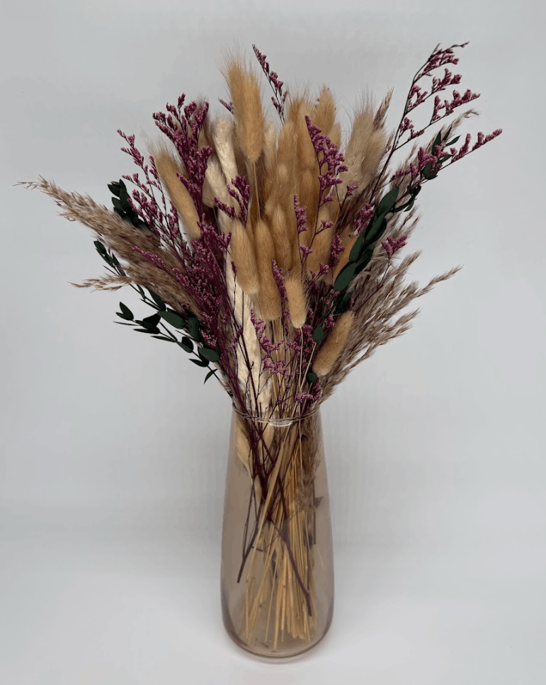 Angled view of boho dried flower arrangement with pampas grass, pink dried flowers, and eucalyptus in a clear glass vase on a white background