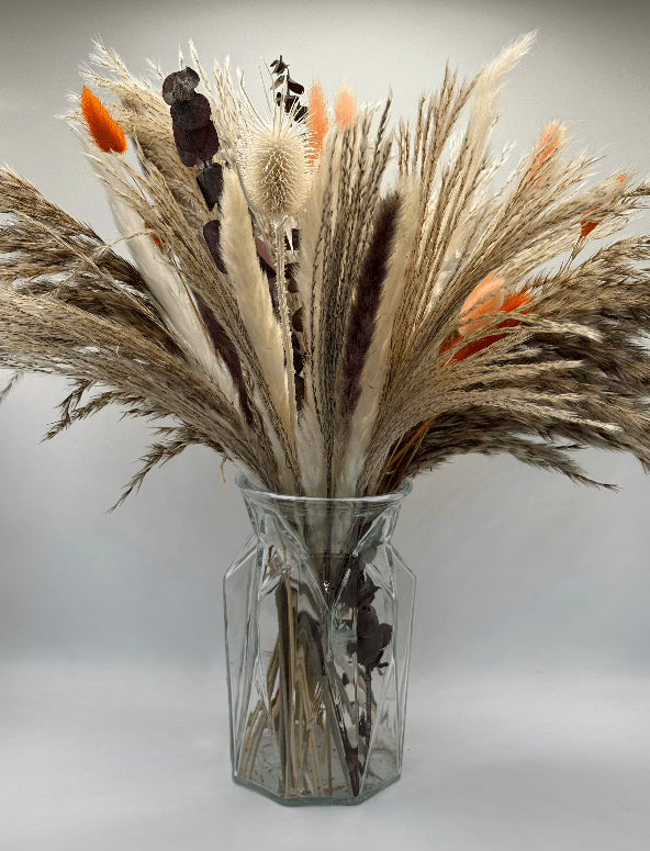 Clear glass vase with dried plants on a light gray background