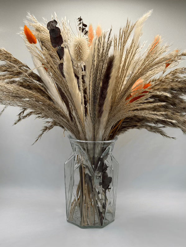 Clear glass vase with dried grasses and flowers on a light gray background