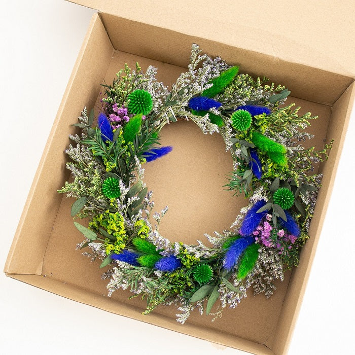 Decorative wreath with green and blue flowers in a cardboard box