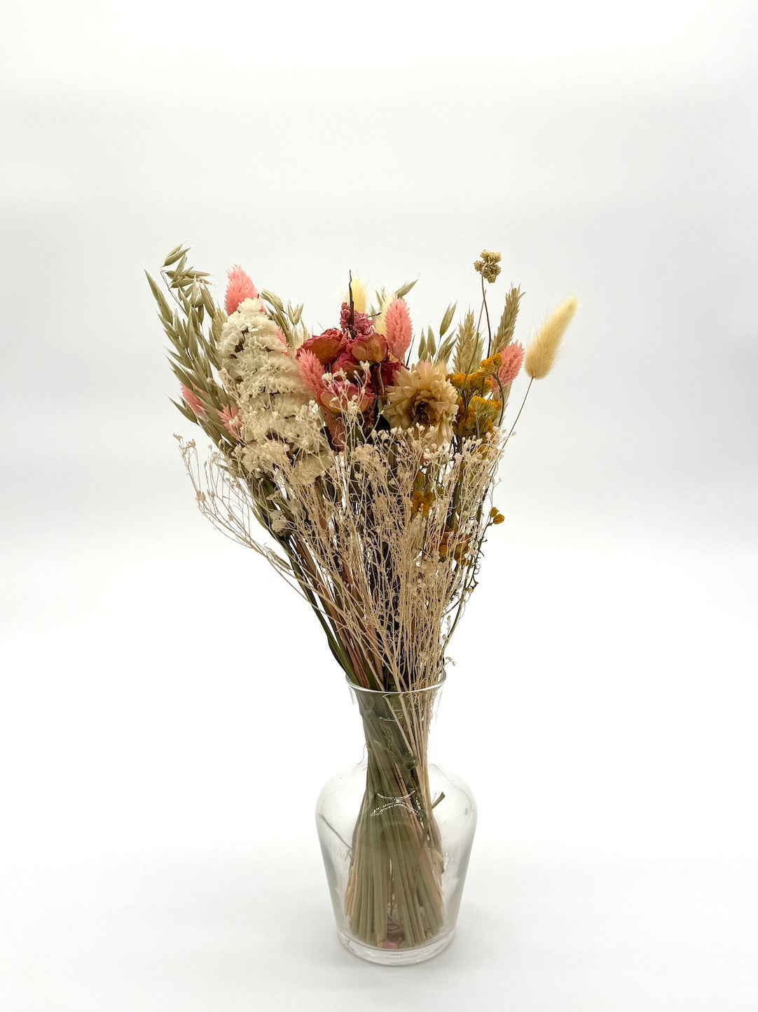 Bouquet of dried flowers in a clear glass vase on a white background
