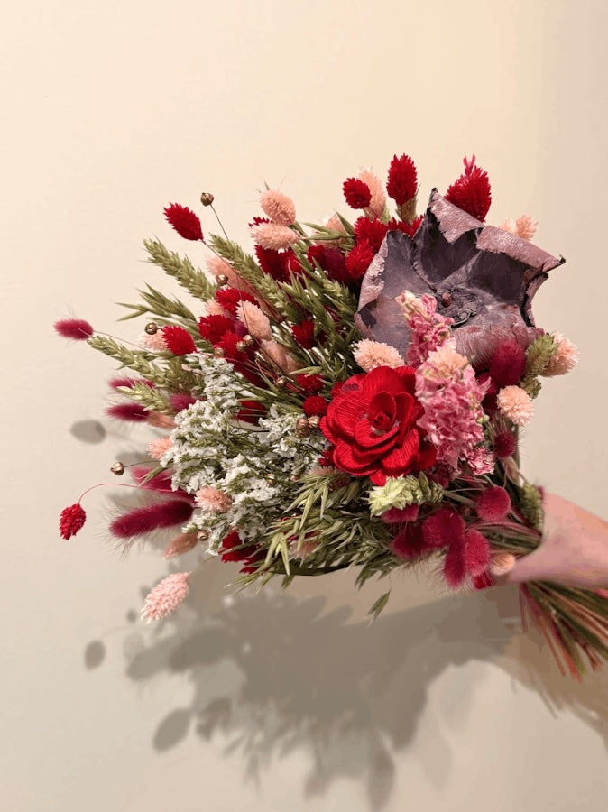 Bouquet of red and pink flowers held against a plain background