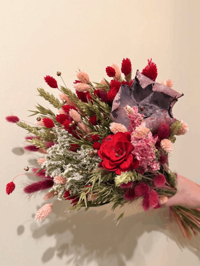 Bouquet of red and pink flowers held against a beige background
