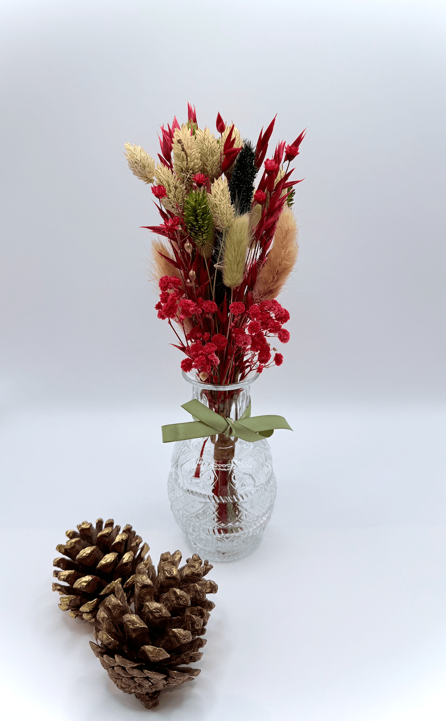 Glass vase with dried flowers and a pine cone on a white background