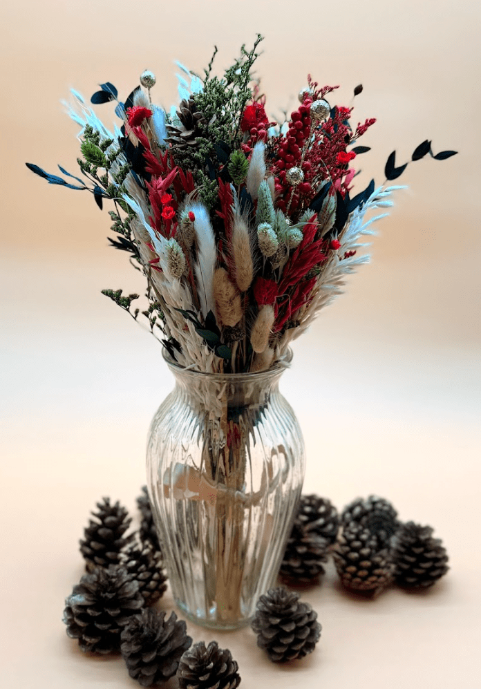 Decorative vase with dried flowers and pinecones on a light background