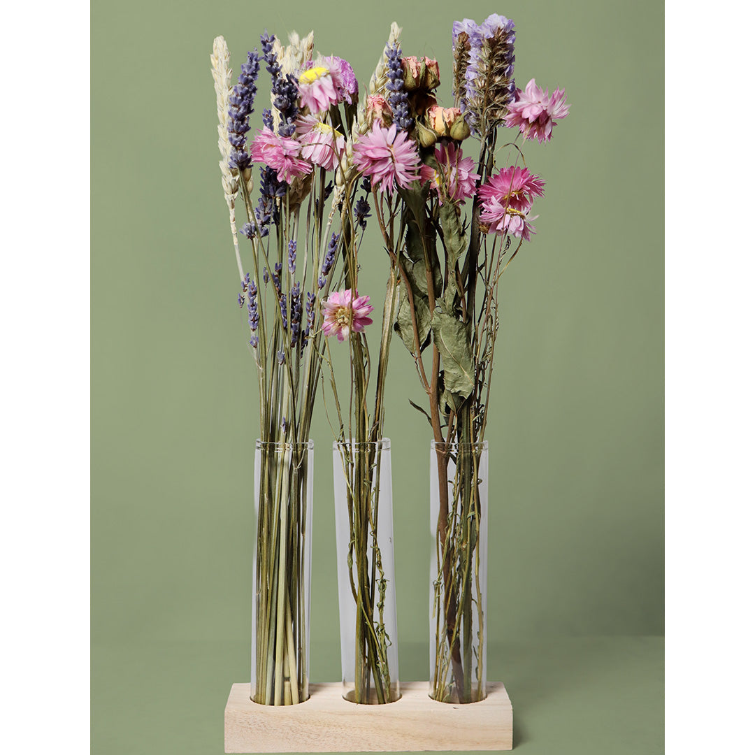 Three clear glass vases with dried flowers on a green background