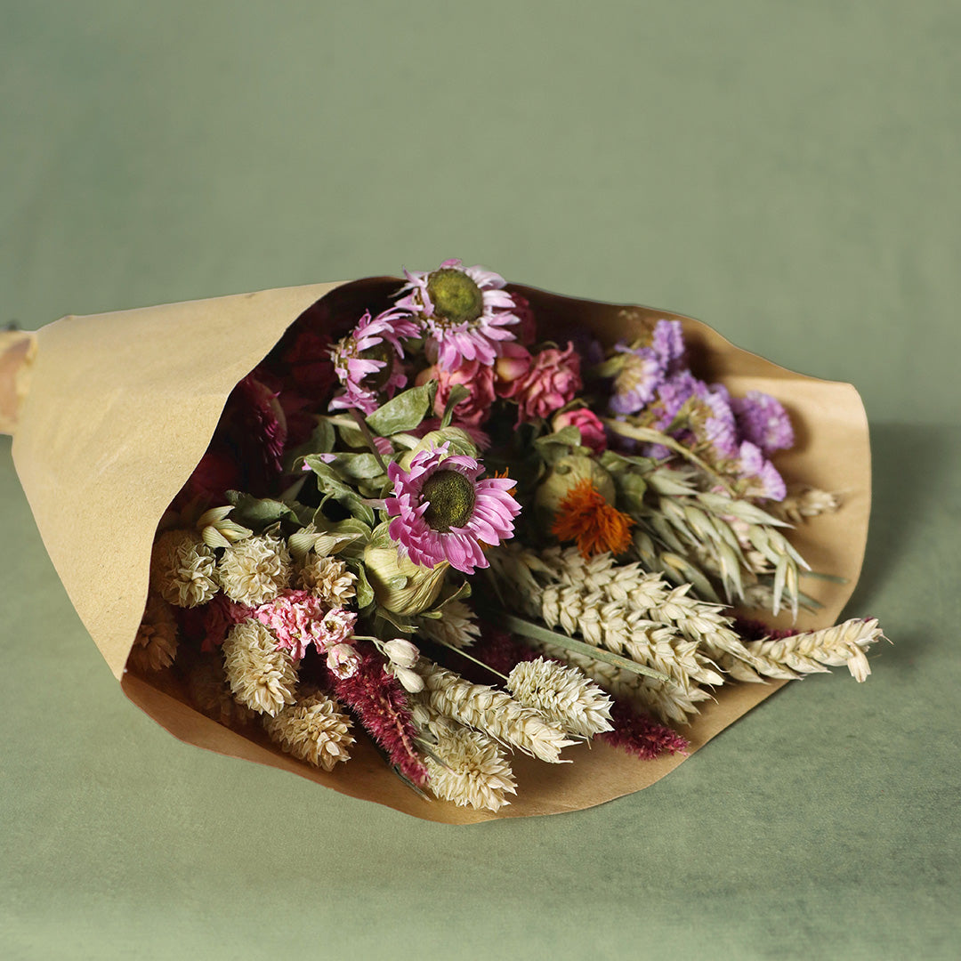 Bouquet of dried flowers wrapped in brown paper on a green background