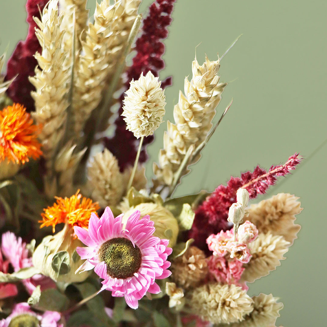 Bouquet of dried flowers with a pink flower in the foreground on a green background