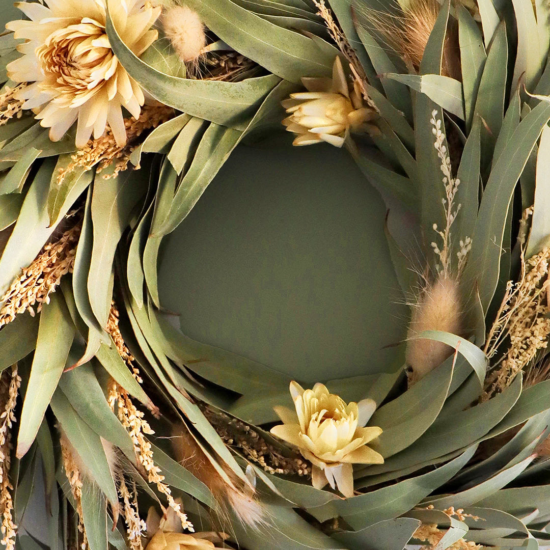 Decorative wreath with green leaves, yellow flowers, and dried grasses on a dark background