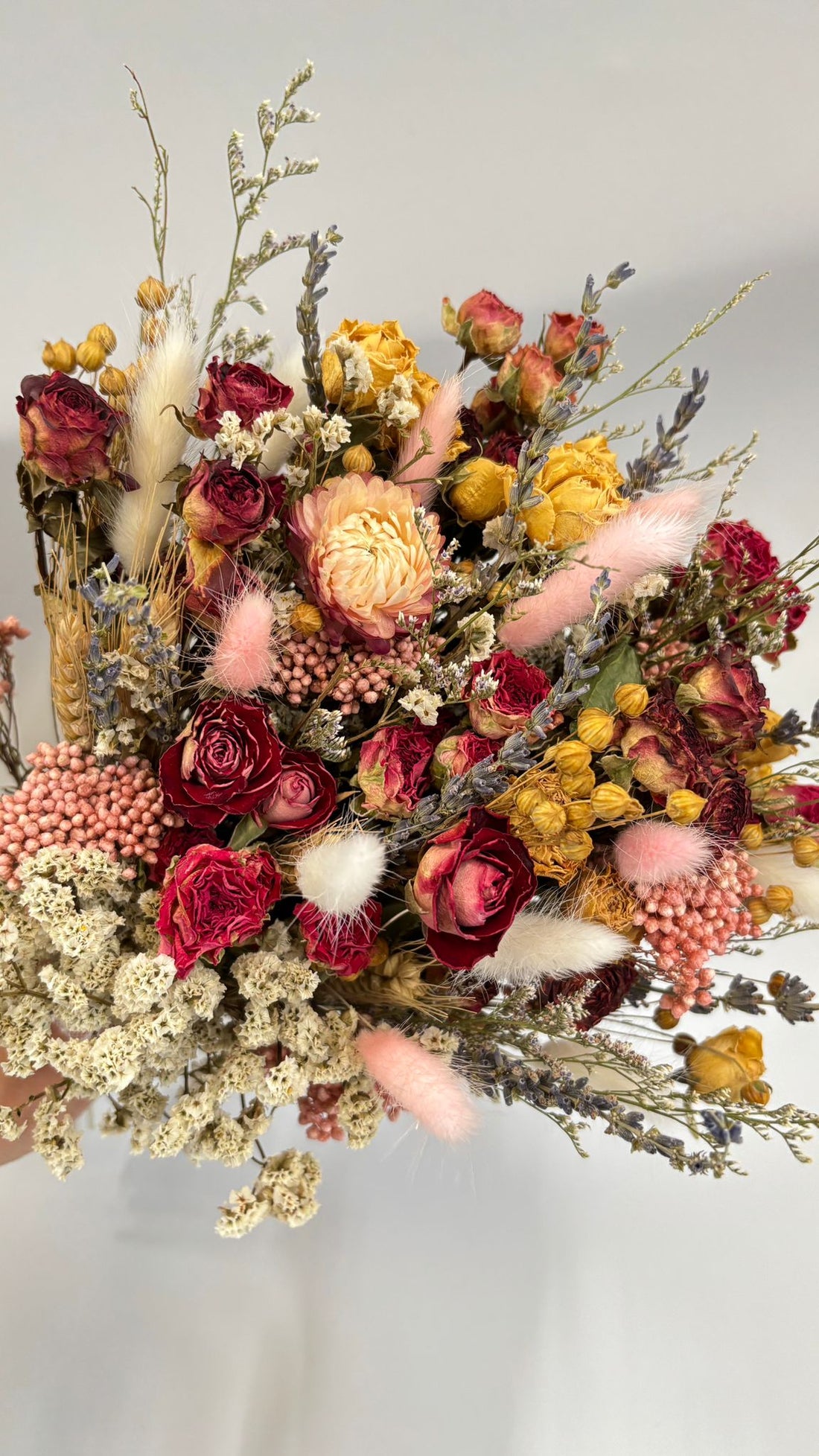 Bouquet of dried flowers with red, pink, and yellow colors on a light gray background