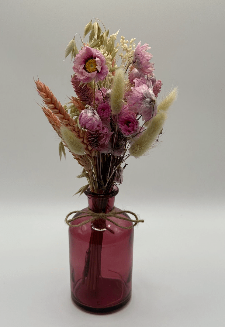 Pink glass vase with dried flowers on a white background