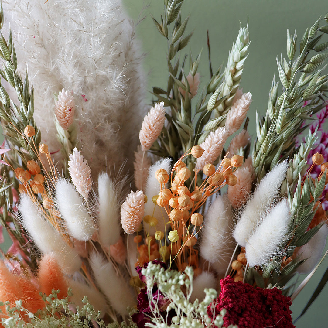 Bouquet of dried flowers with white, orange, and green elements on a light green background