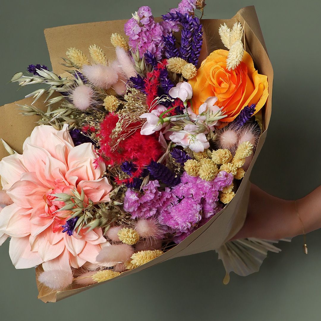Bouquet of colorful flowers wrapped in brown paper against a dark background