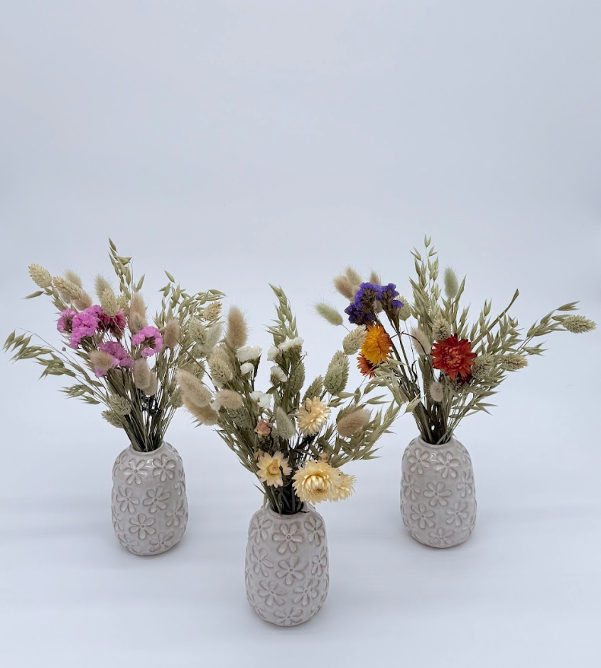 Three textured ceramic vases with dried flowers on a light gray background