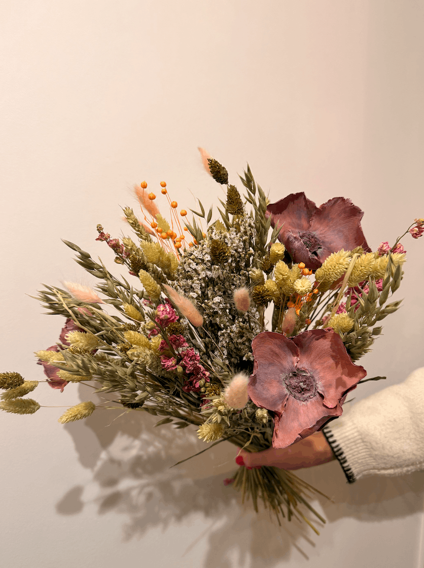 Hand holding a bouquet of dried flowers against a plain background