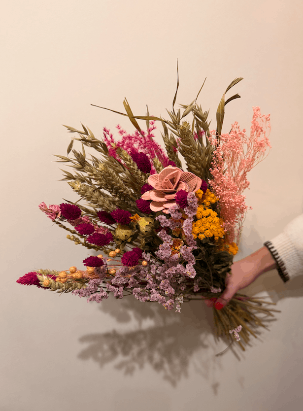 Bouquet of dried flowers held by a person against a plain background