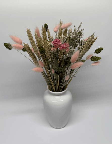 Full view of dried flower bouquet with pink roses, wheat grasses, and pink bunny tails in a white vase on a light grey background