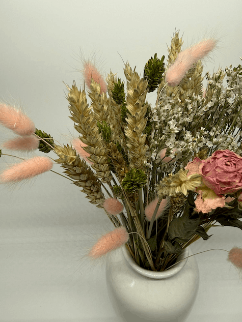 Side view of dried flower bouquet with pink roses, white dried flowers, bunny tails, and wheat grasses in a white vase