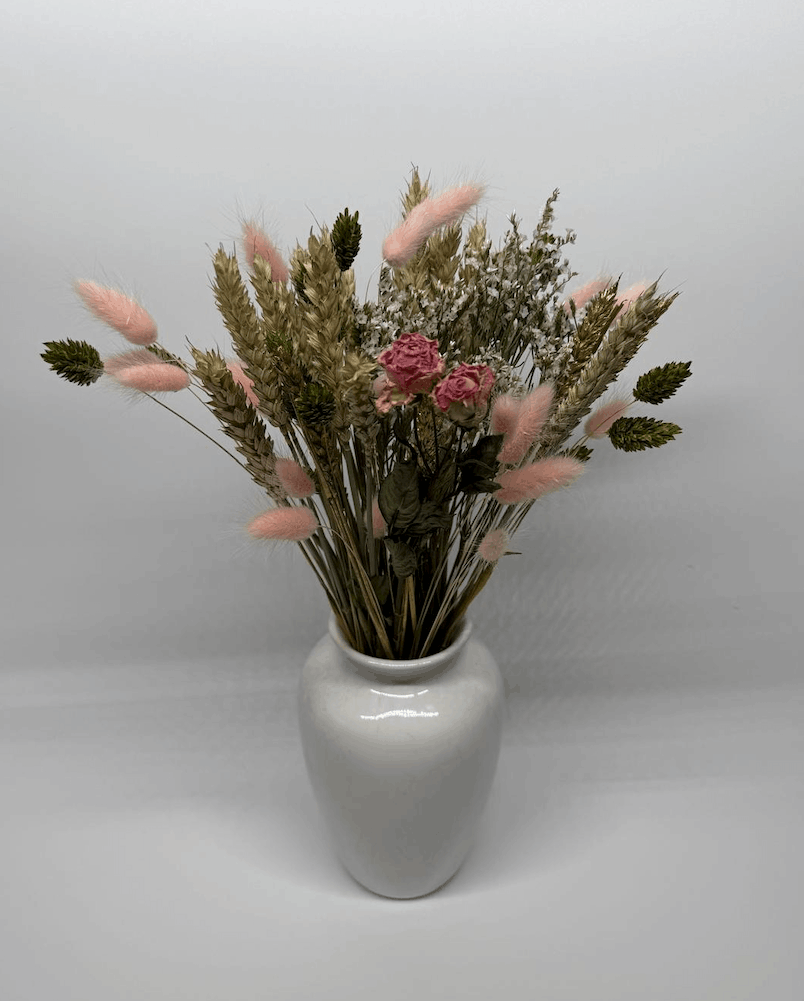Dried flower bouquet with pink roses, wheat grasses, and pink bunny tails in a white vase on a grey background