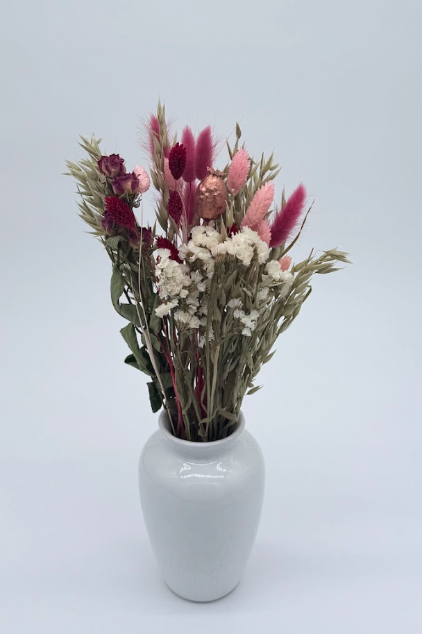 bouquet of dried flowers against a plain background in a white ceramic vase