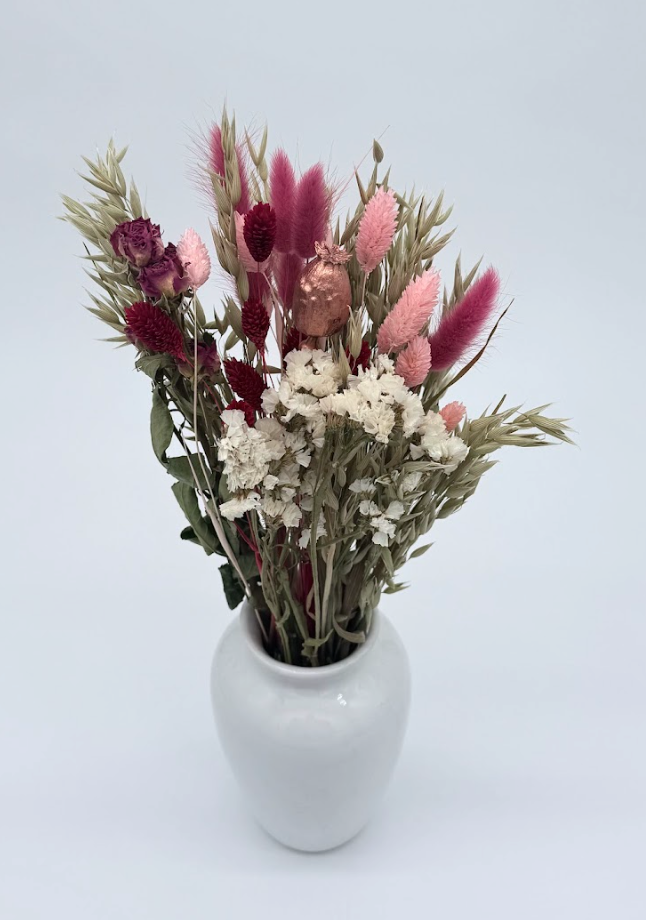 bouquet of dried flowers against a plain background in a white ceramic vase