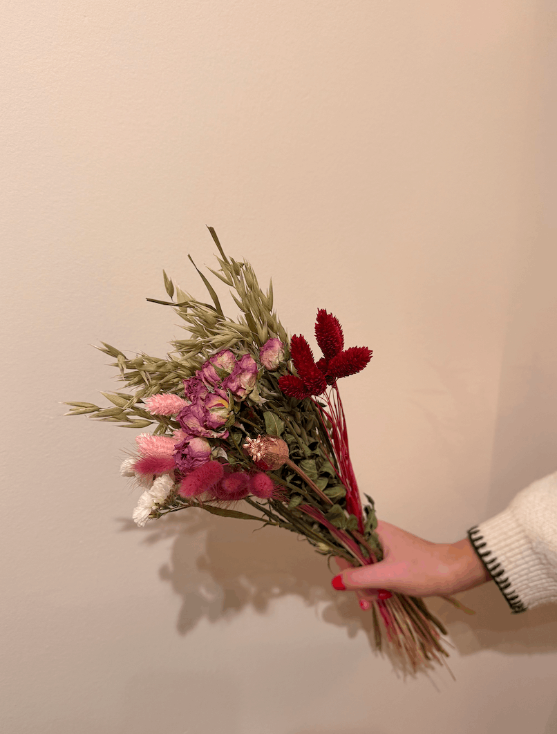 Hand holding a bouquet of dried flowers against a plain background