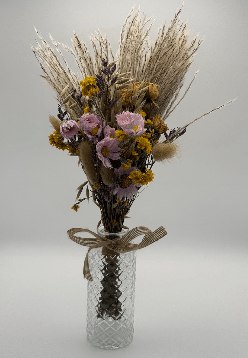 Bouquet of dried flowers and herbs in a glass vase on a light gray background