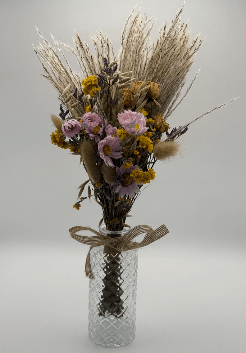 Bouquet of dried flowers in a glass vase with a textured surface on a light gray background