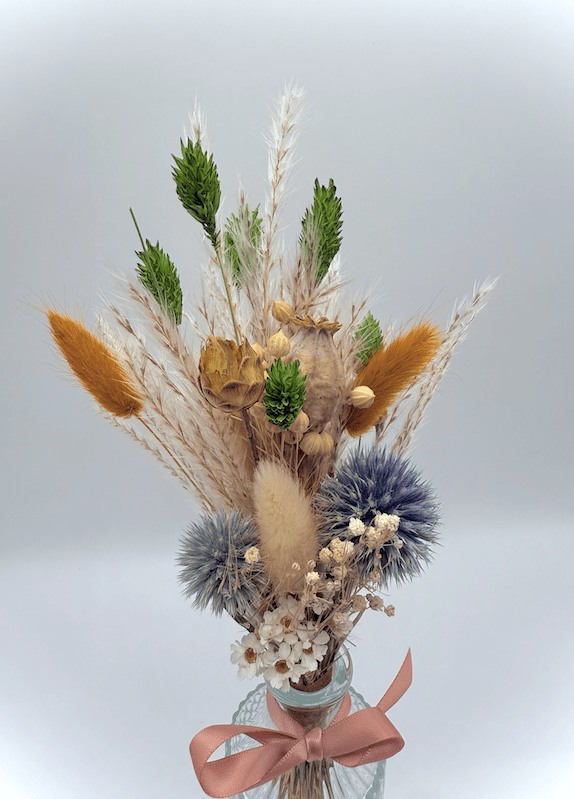 Bouquet of dried flowers with a pink ribbon on a light gray background
