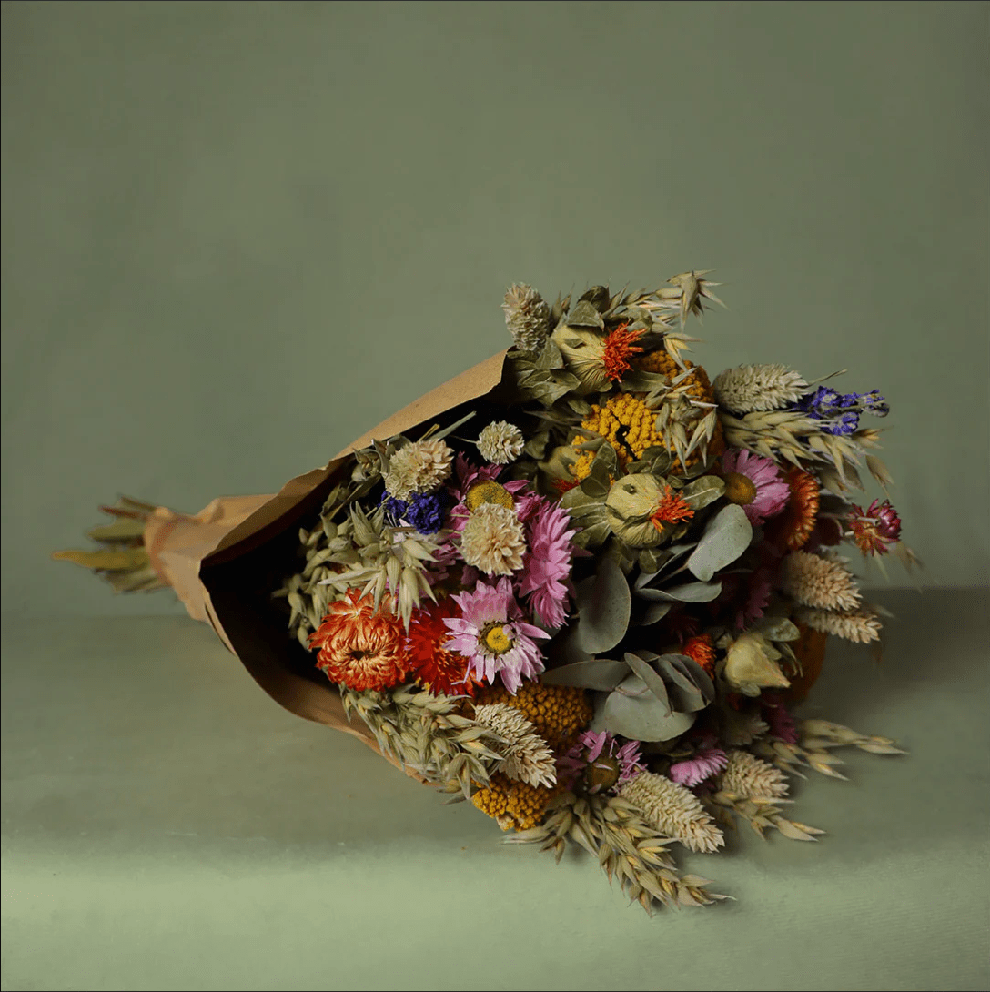 Bouquet of dried flowers in brown paper packaging on a green background