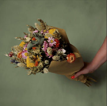 Bouquet of dried flowers wrapped in brown paper held by a hand on a green background